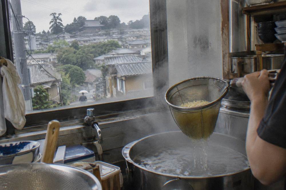 Fresh ramen noodles being lifted from boiling water in a kitchen pot