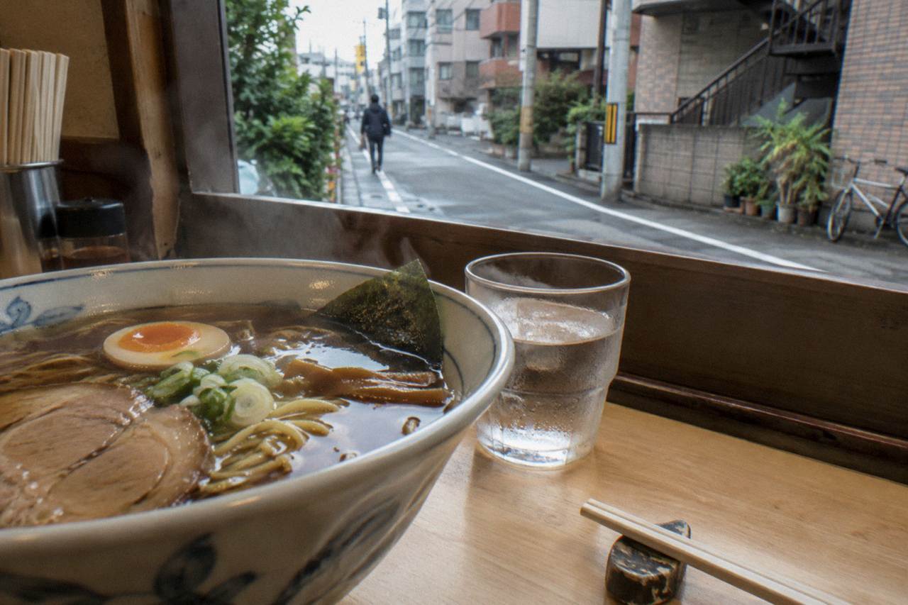 Steam rising from a bowl of shoyu ramen on a wooden counter beside chopsticks