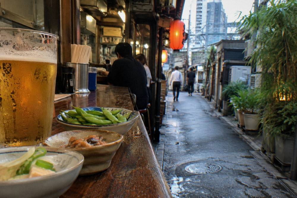Small plates of Japanese food lined up along a wooden bar in a narrow eatery