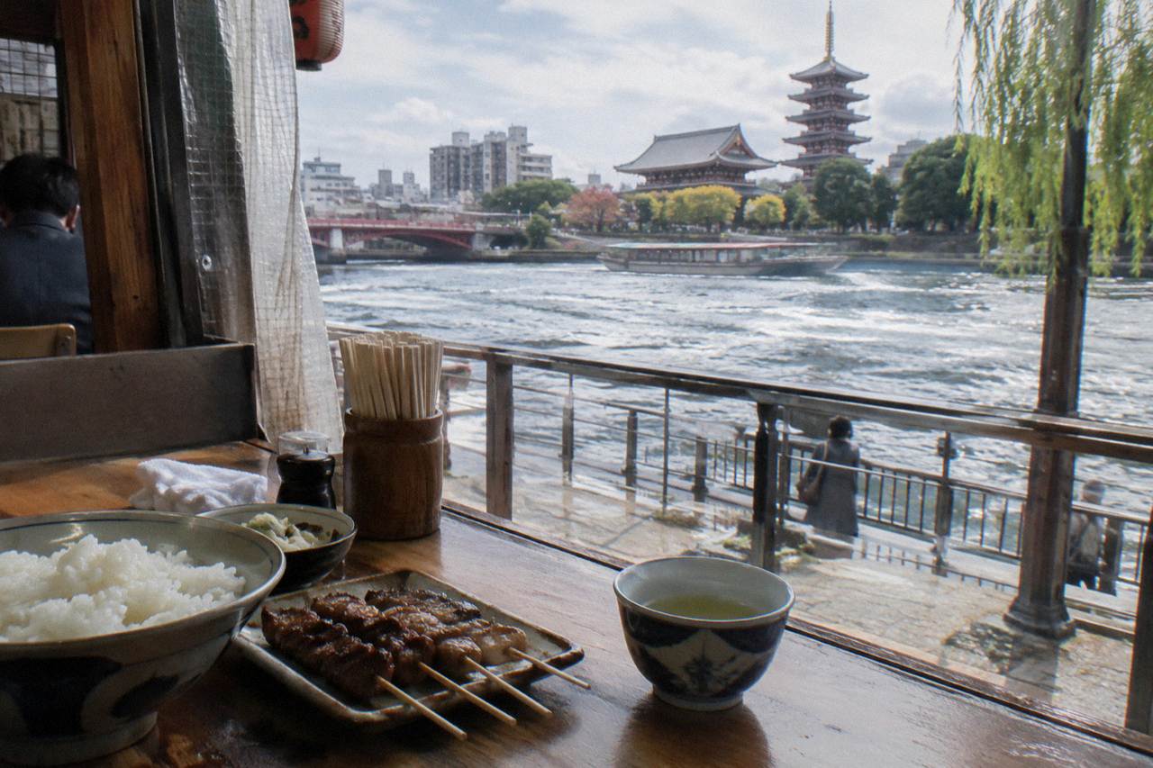 A wooden counter in a small Tokyo eatery with bowls of rice and grilled skewers set on it