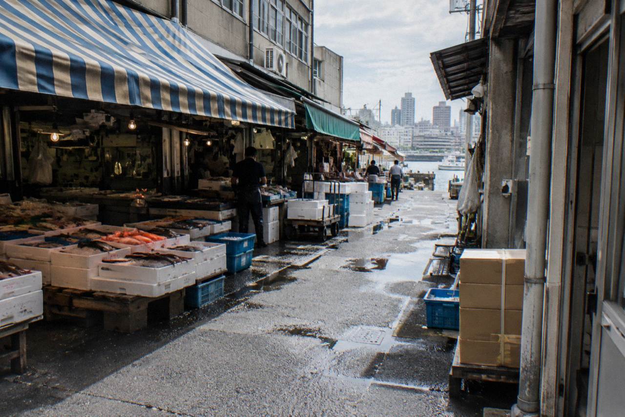 Narrow market lane lined with small seafood stalls and hanging shop signs under awnings