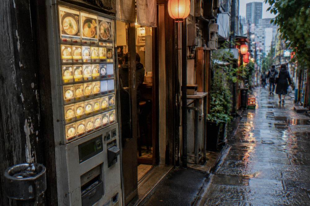 A ramen counter ticket machine with small wooden trays in a compact Tokyo shop
