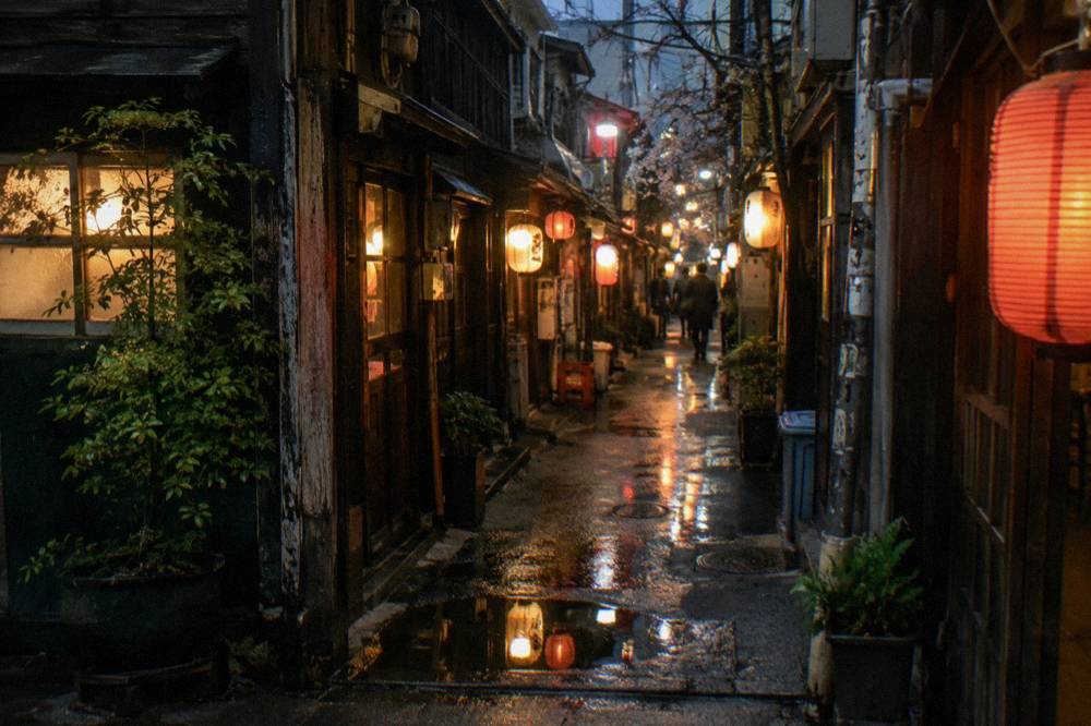 Rows of glowing lanterns lining a narrow alley entrance at night