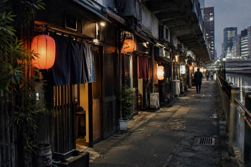 A row of illuminated restaurant signs and lanterns along a narrow lane of small bars in Ginza at night