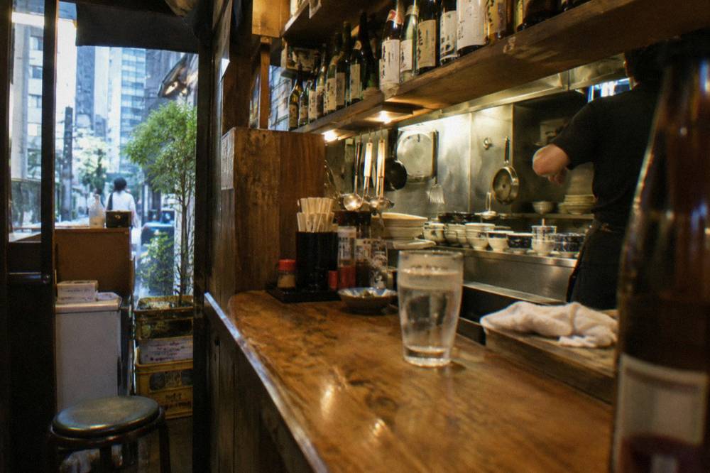 Interior of a small Shinjuku izakaya with bottles lined along a wooden counter