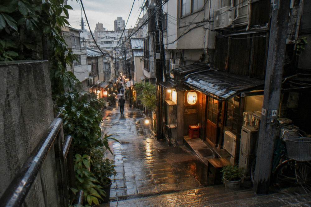 A narrow lantern-lit alley of small bar entrances in the evening