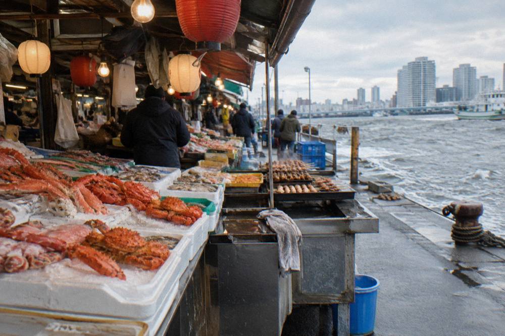 Stacks of fresh seafood and skewered snacks displayed on a crowded market stall under hanging lanterns