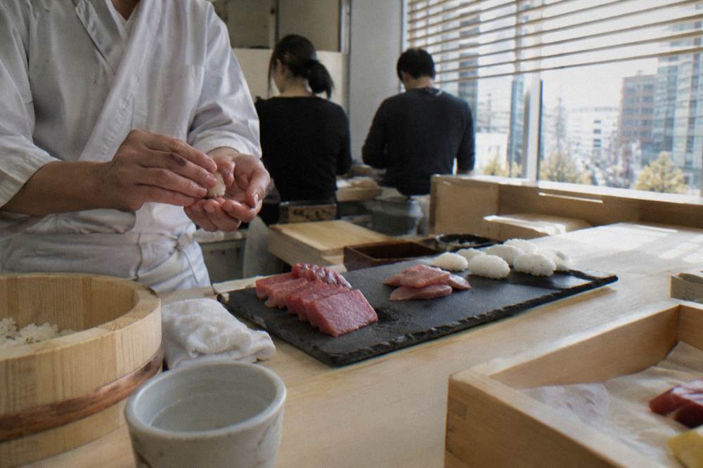 Hands shaping rice and fish into nigiri sushi at a wooden counter