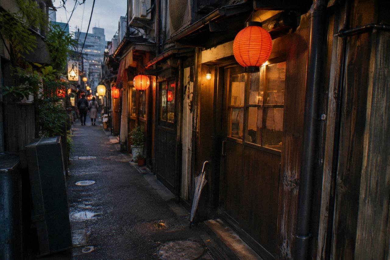 A narrow Tokyo alley at dusk with lanterns glowing above small restaurant entrances