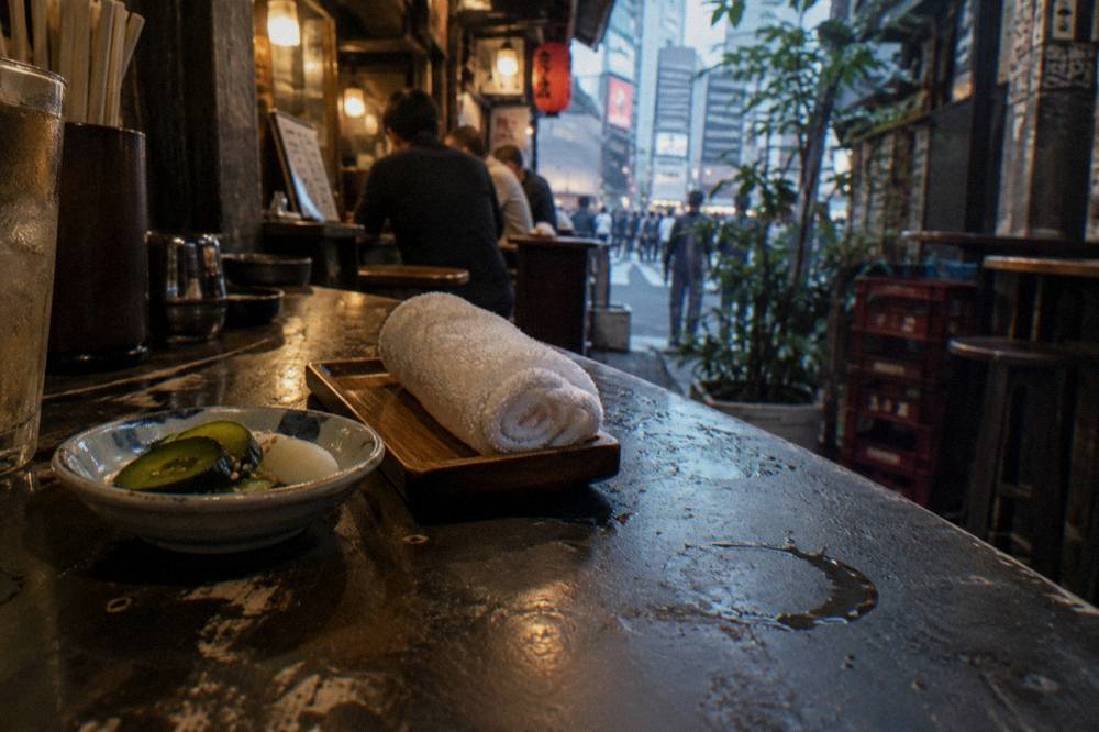 Close view of a wooden tray holding a small appetizer dish and a wet towel on a dark restaurant counter