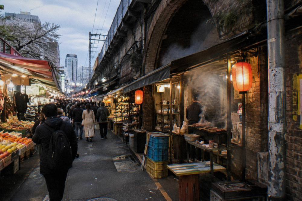 Charcoal smoke rising from tiny grill counters packed along a narrow lantern-lit alley