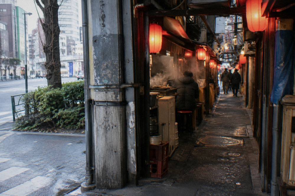 A row of tiny grill-front yakitori counters glowing under red lanterns in a narrow Shinjuku alley