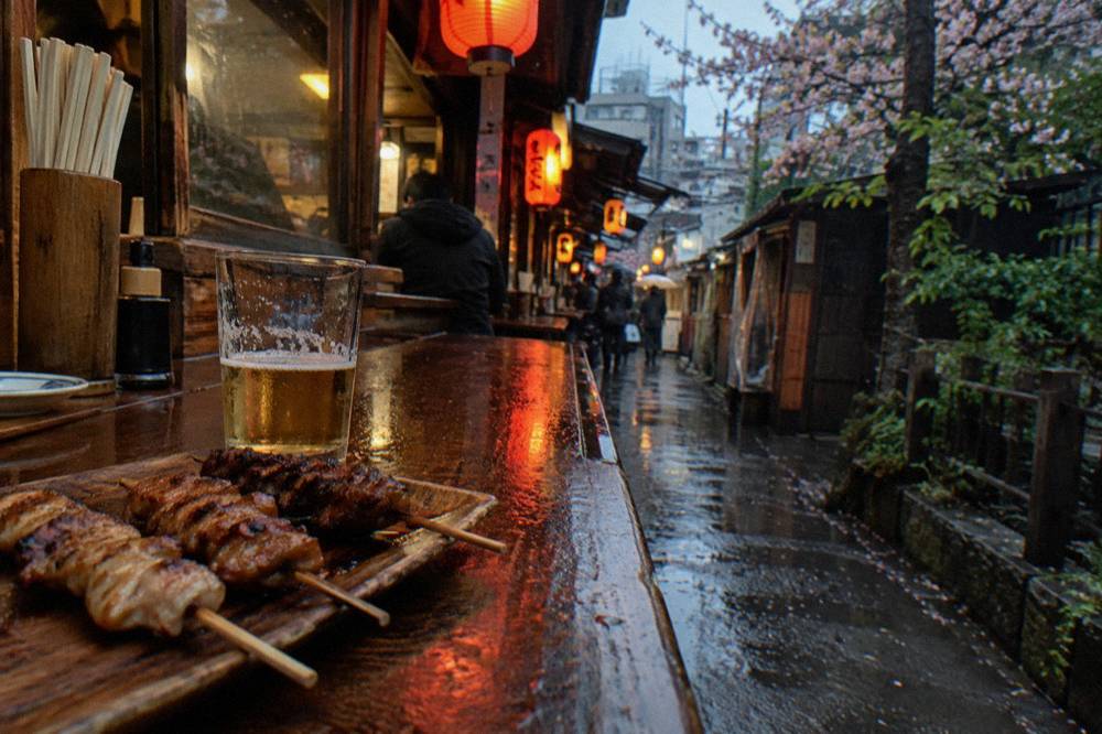 Grilled yakitori skewers arranged on a wooden tray beside a small glass of beer