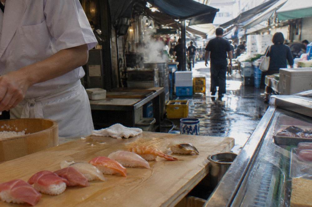 Fresh nigiri sushi pieces resting on a wooden counter in front of a chef's workspace