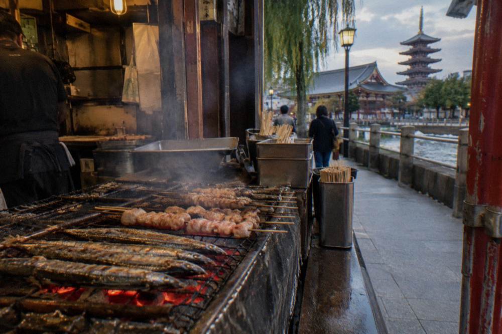 Grilled skewers cooking over charcoal at a narrow stall counter