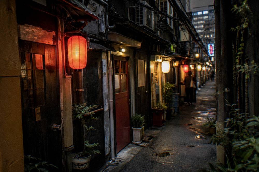 Narrow Golden Gai lane of tiny bars with glowing lanterns after dark