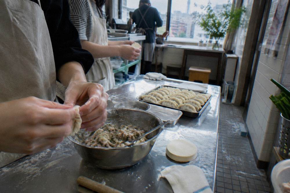 Hands folding gyoza dumplings on a floured table in a cooking class kitchen