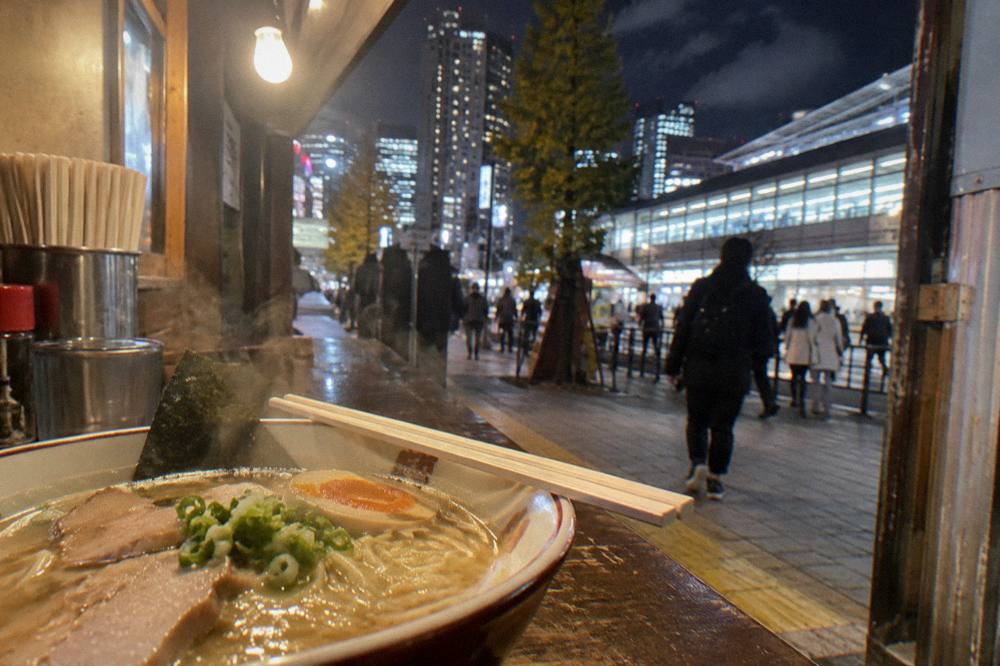 Bowl of ramen with sliced pork, egg and nori on a counter beside chopsticks