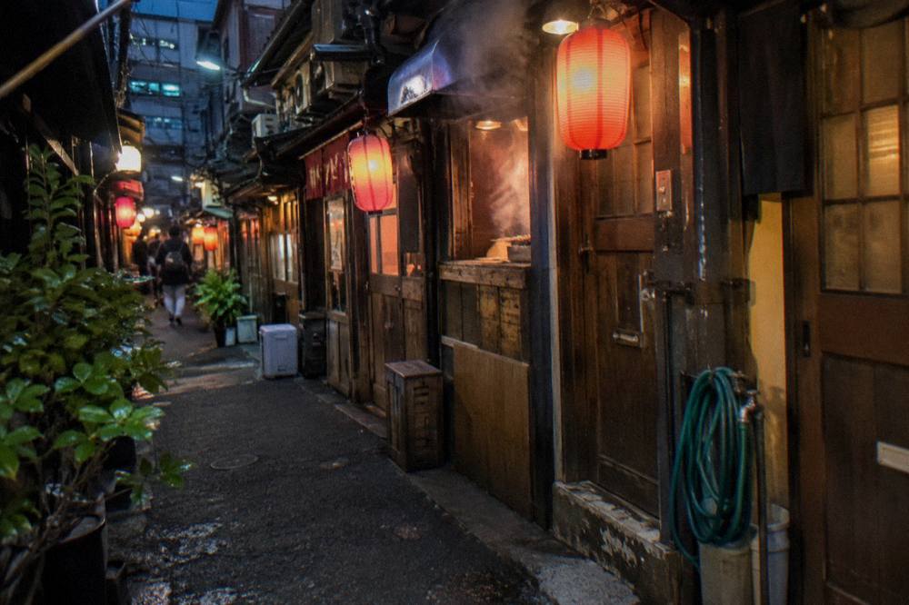 Narrow lantern-lit alley of small yakitori counters with smoke rising from grills at night
