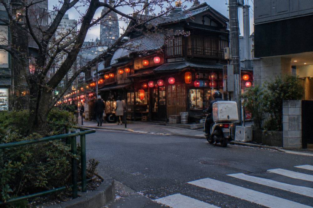 Busy izakaya street in Shibuya at dusk with red lanterns and glowing shop signs