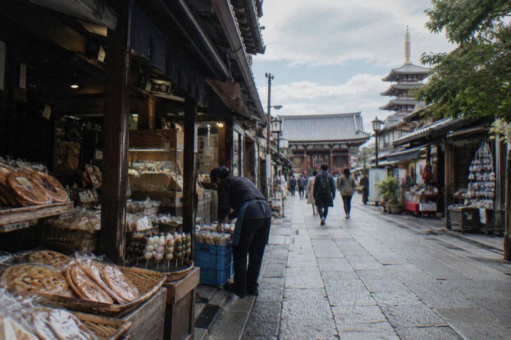 Traditional shopping street in Asakusa with wooden storefronts and food stall displays in daylight