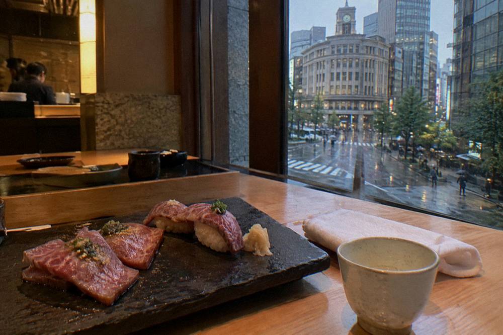 Sliced premium wagyu beef and prepared sushi arranged together on a slate serving board