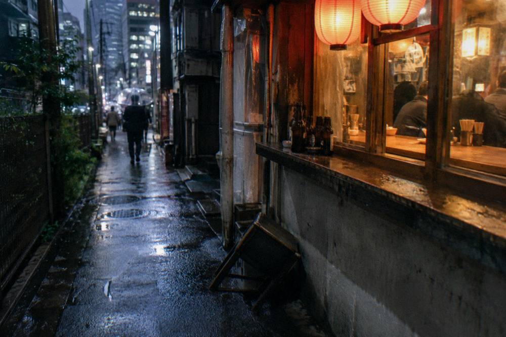 Small izakaya counter with lanterns glowing over a Shinjuku side street at night