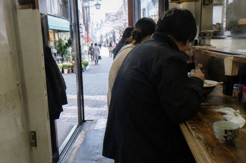 Standing bar counter with customers eating closely side by side in a compact Tokyo shop