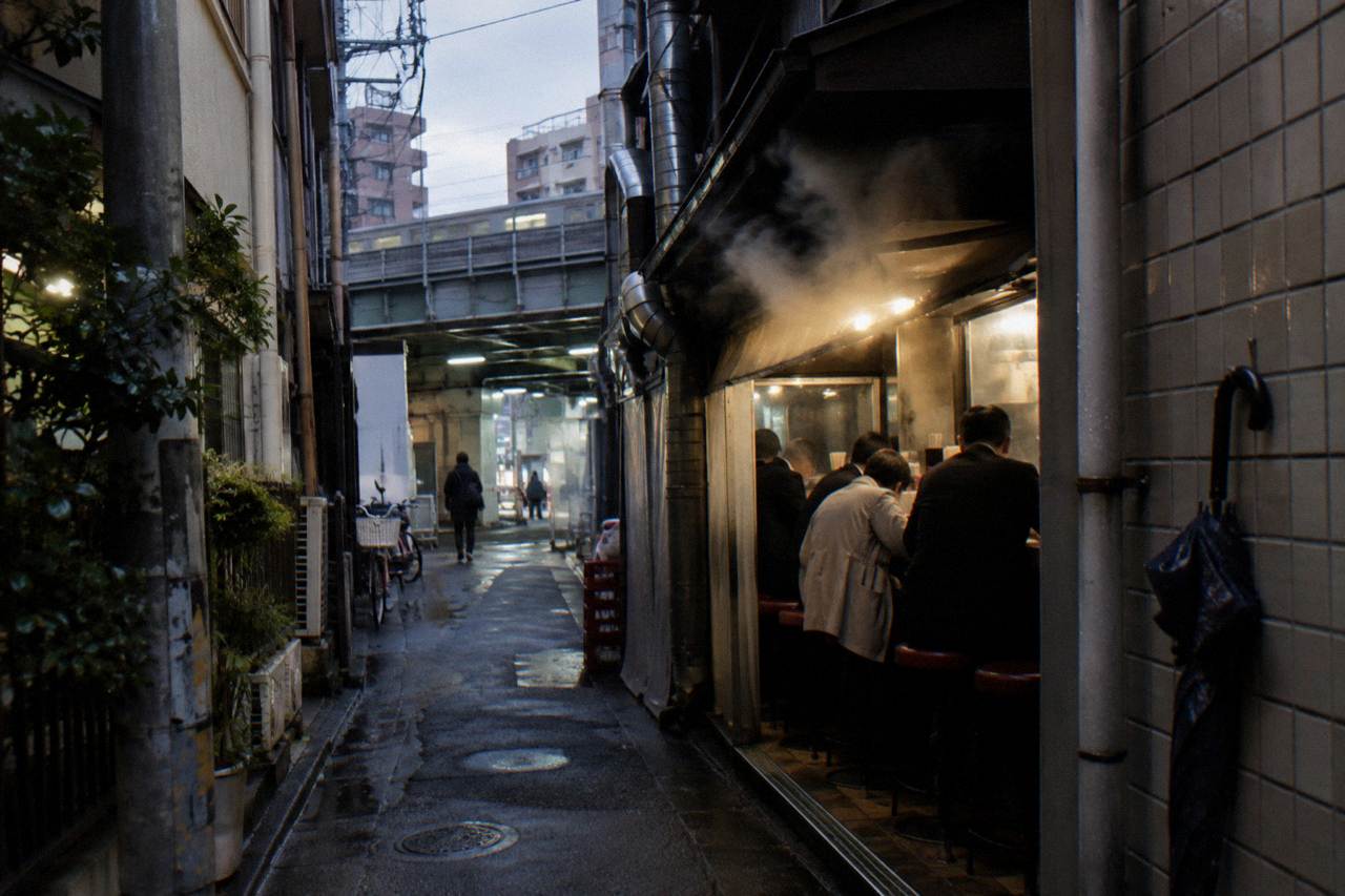 Steam rising from a small counter shop lantern-lit alley in Tokyo at dusk