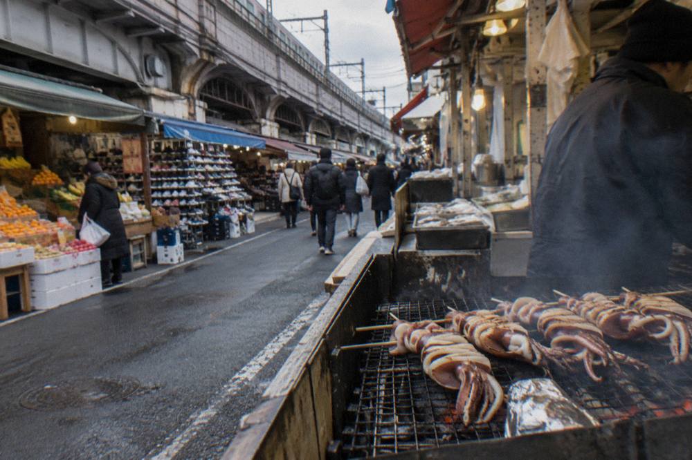 Small grill counter with smoke rising over skewers in a narrow market alley