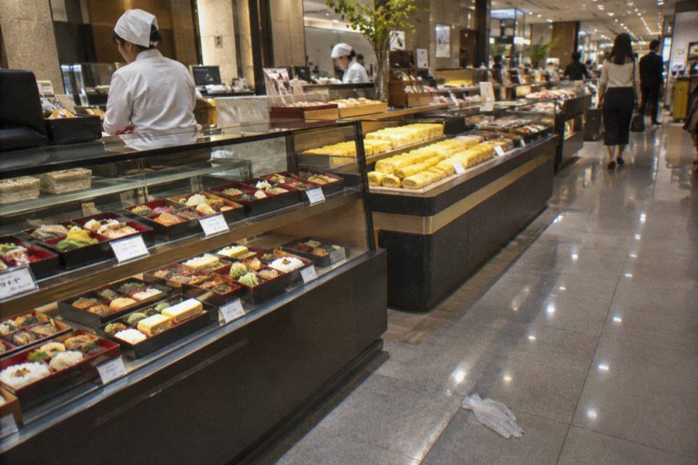 Depachika basement food hall counters with trays of prepared dishes under bright display lighting