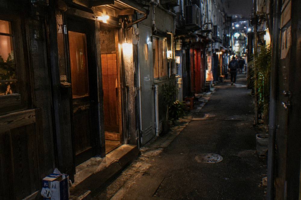 Row of small bar entrances with glowing lanterns along a narrow Golden Gai alley