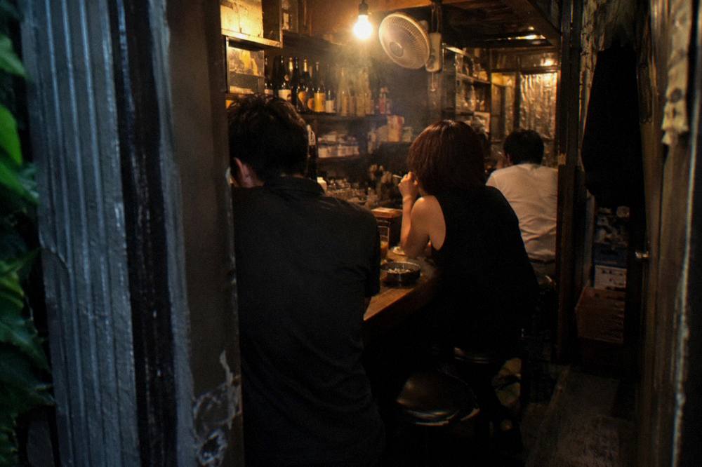 Guests seated at a tiny wooden bar counter talking with a bartender