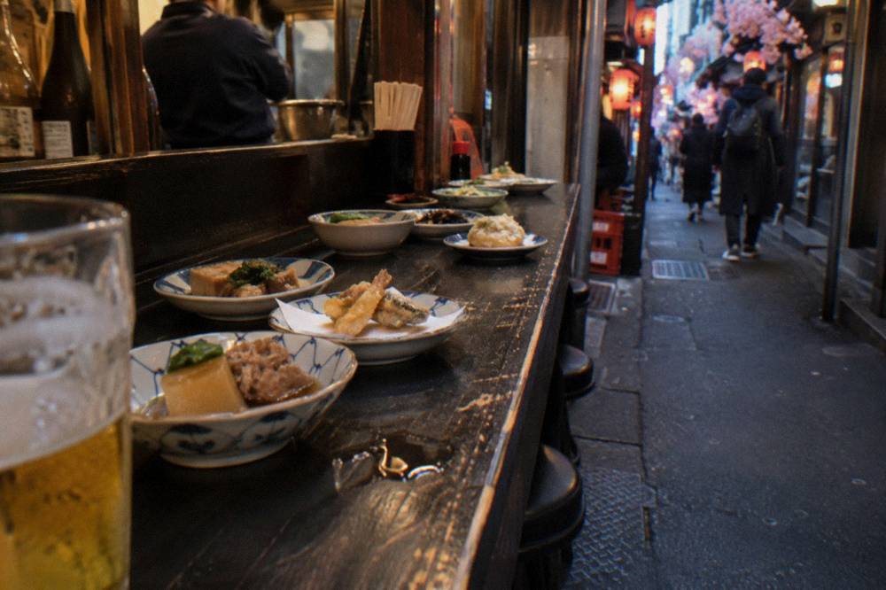 Small plates of Japanese food arranged along a wooden counter in a Tokyo eatery