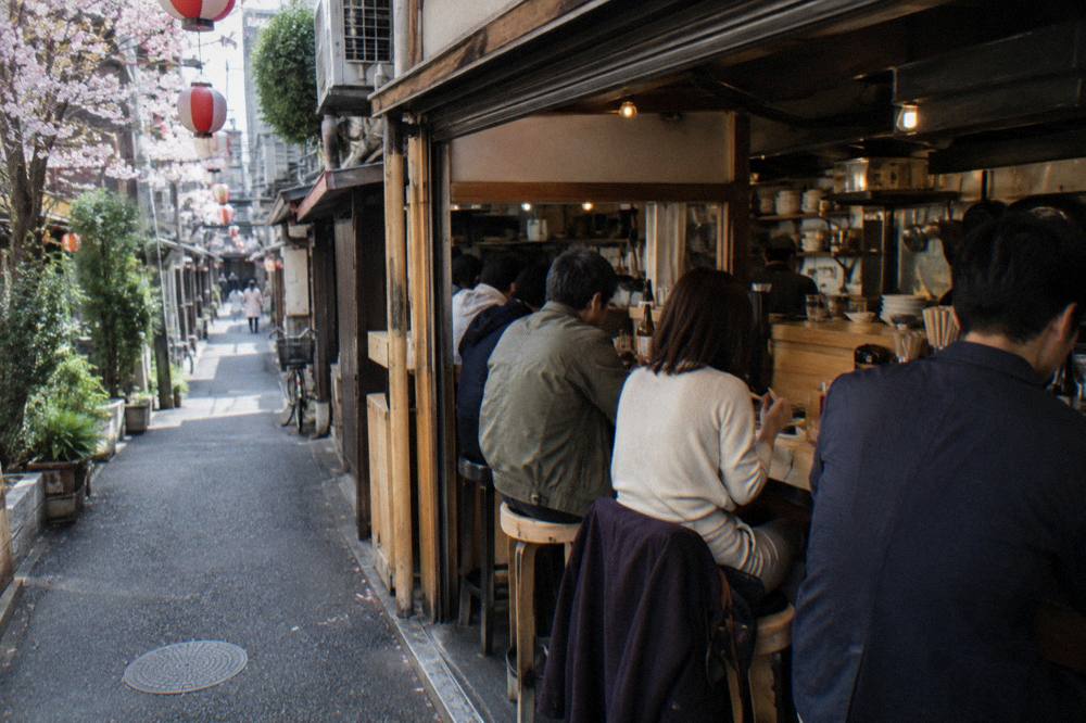 Group of diners seated at a bright counter inside a small Tokyo eatery