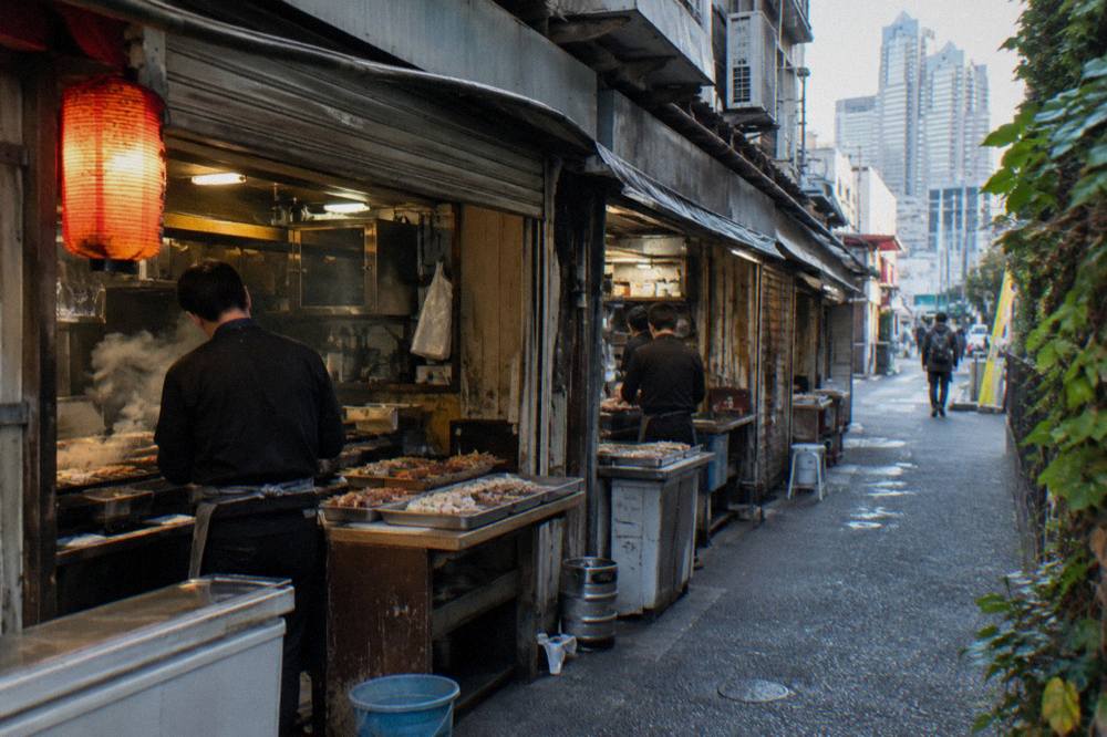Row of tiny open-fronted grill counters glowing under red lanterns at dusk