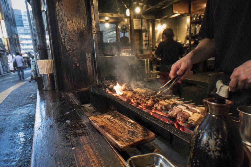 Skewers grilling over charcoal at a small counter with a chef working the grill