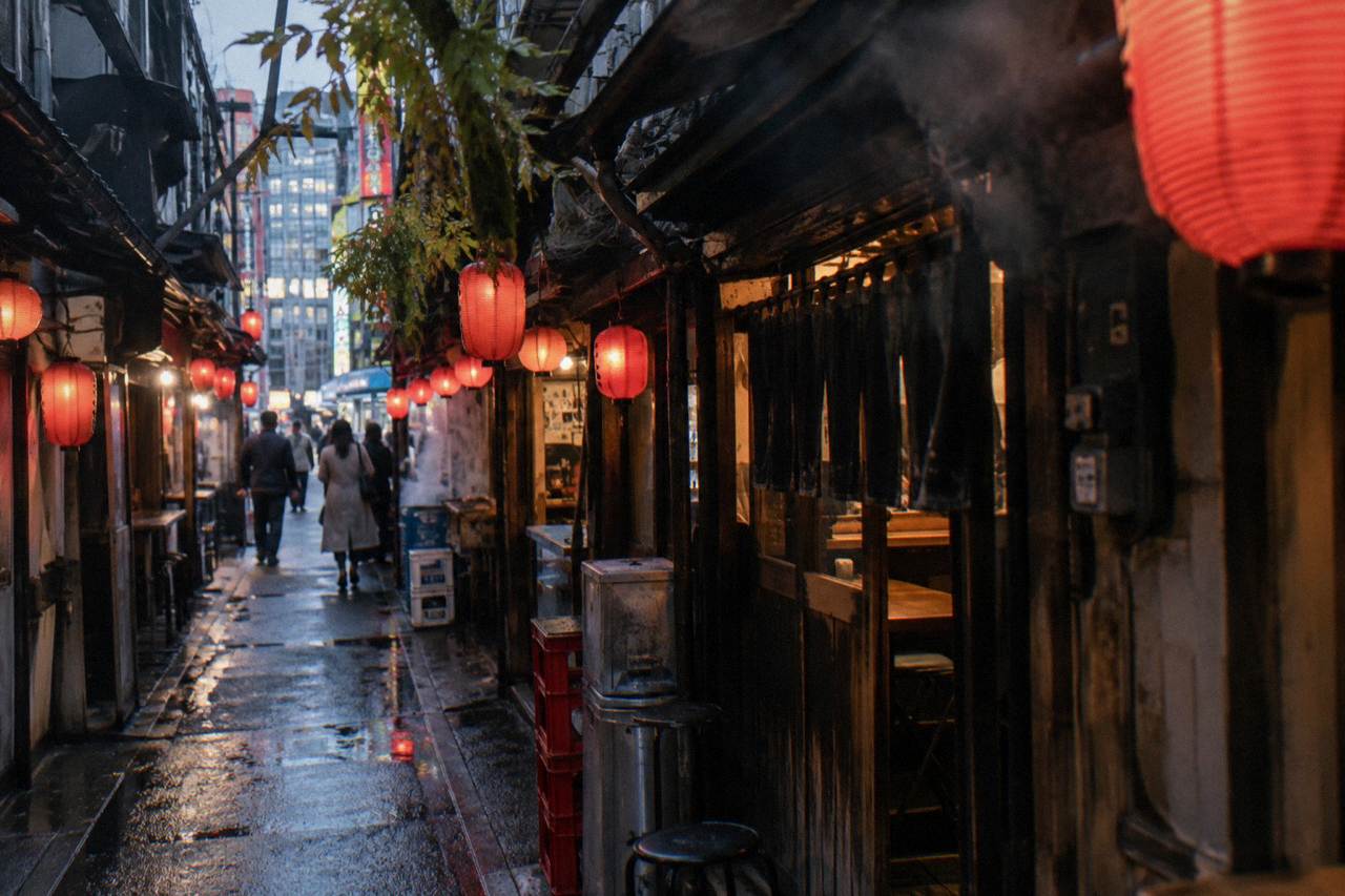 Narrow lantern-lit alley of tiny yakitori counters with smoke drifting between wooden storefronts
