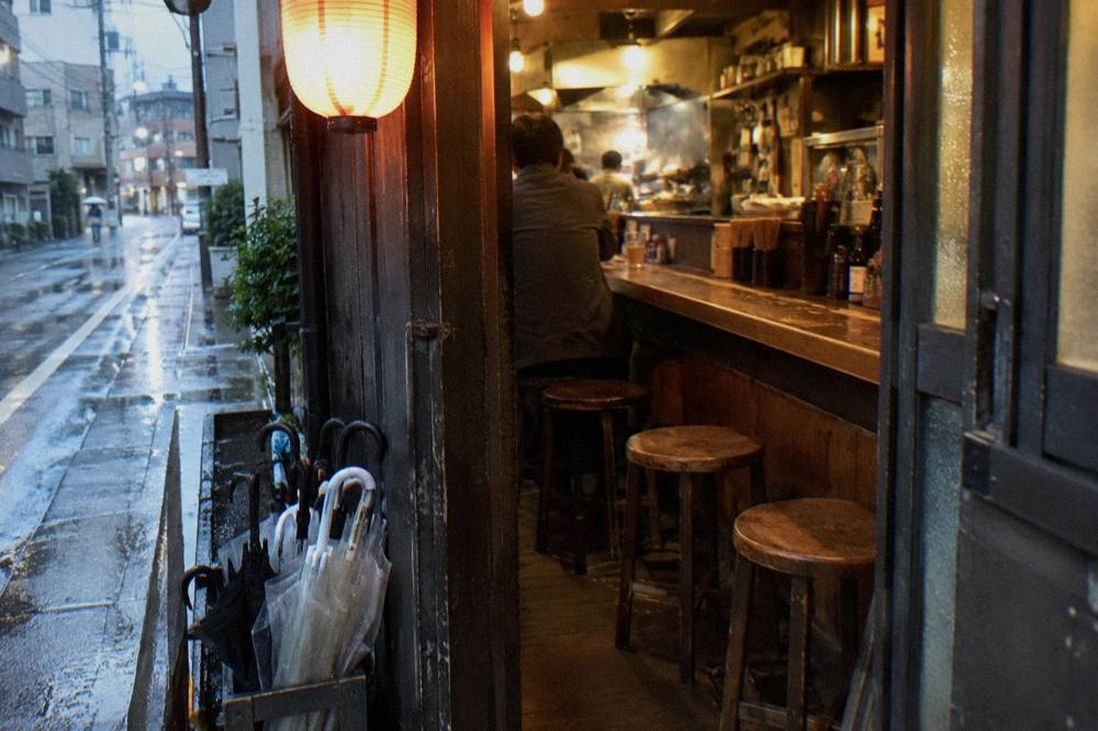 Small izakaya counter interior with wooden stools and hanging lanterns