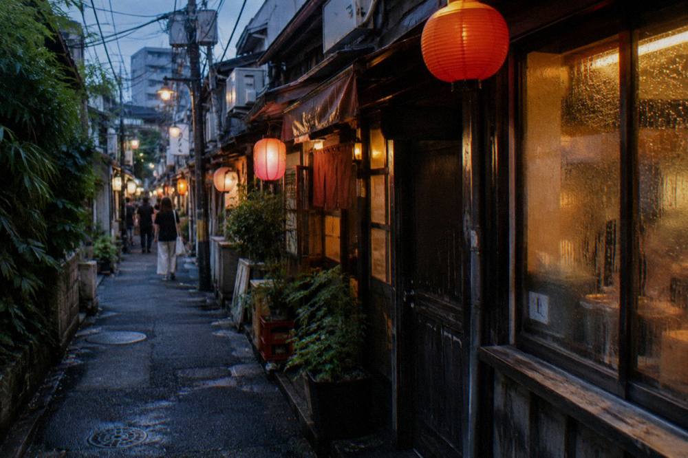 Row of tiny lantern-lit bar fronts along a narrow pedestrian alley in the evening