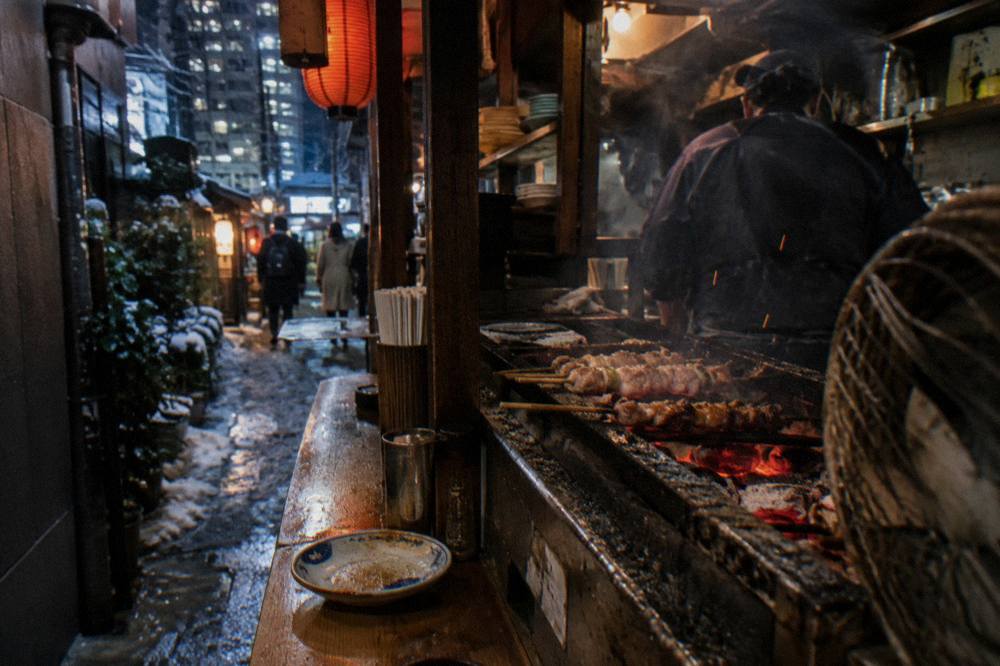 Small grill counter in a narrow Shinjuku restaurant with skewers cooking over charcoal