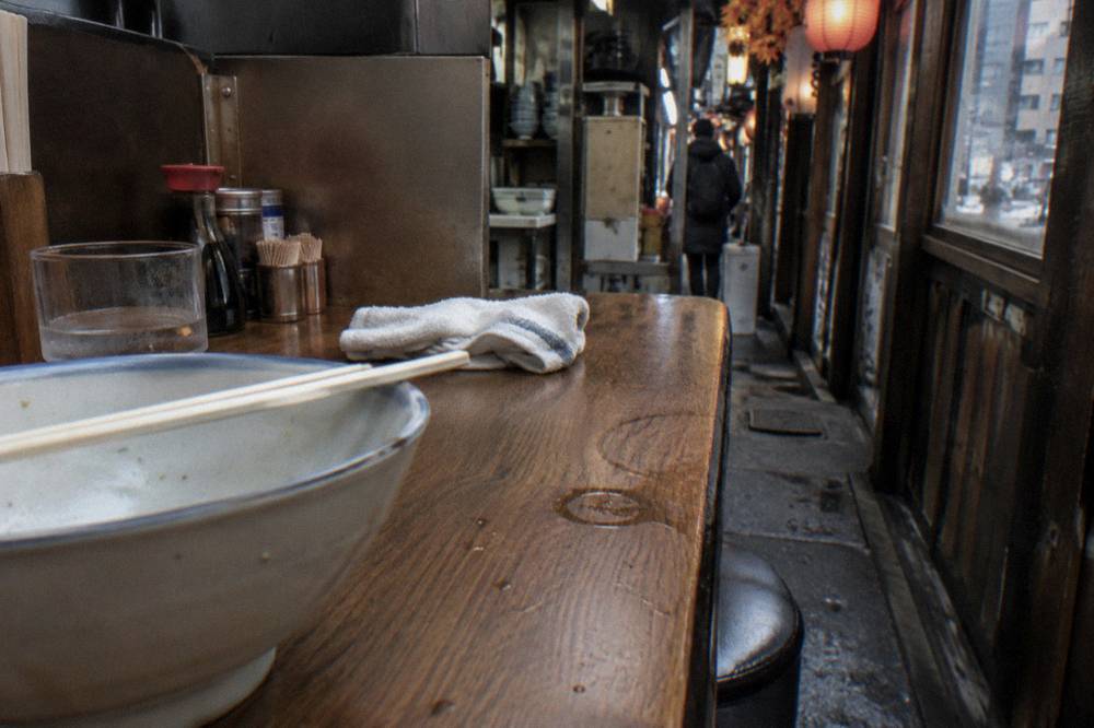Chopsticks resting on a bowl at a wooden counter in a small Japanese restaurant