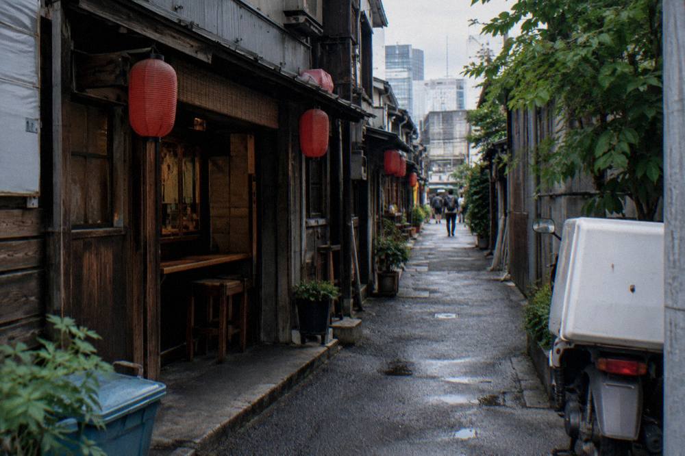 A row of small izakaya counters with red lanterns along a narrow Shinjuku lane at dusk
