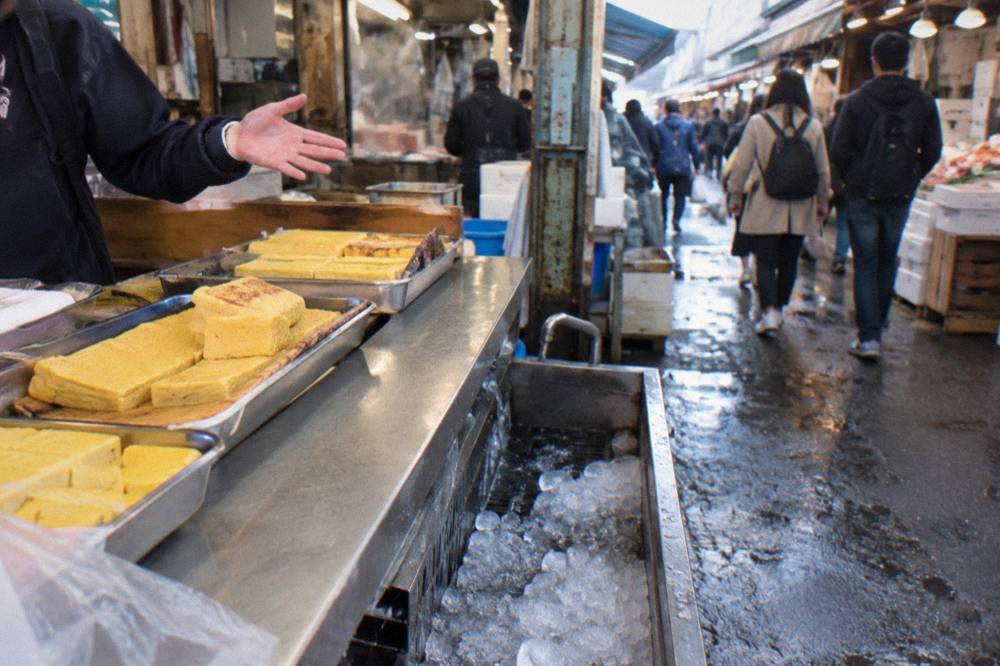 A guide pointing out dishes at a busy counter while a small group tastes skewers
