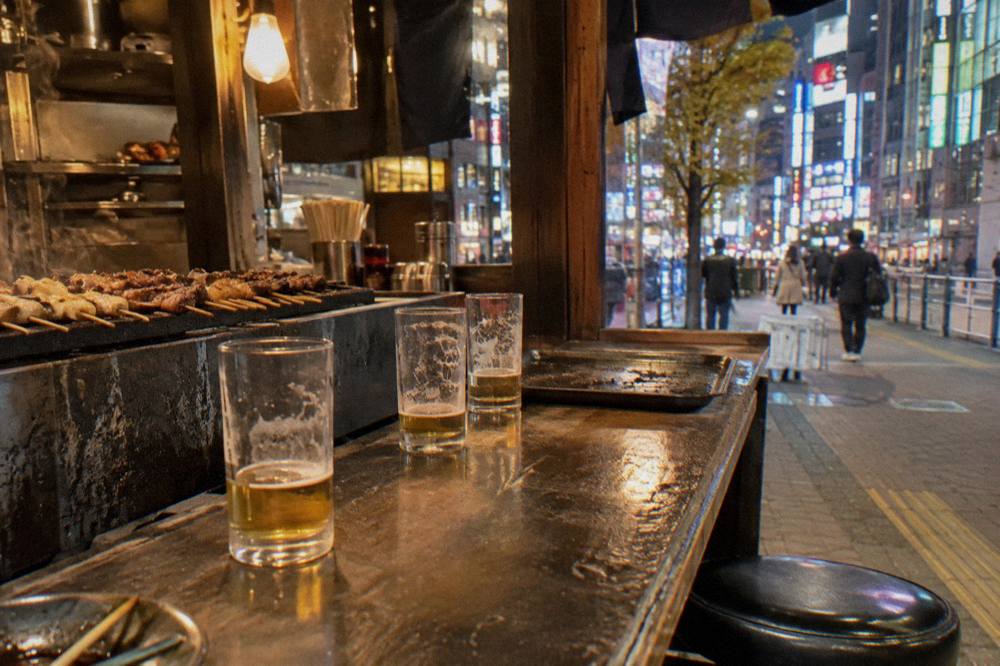A small izakaya counter with grilled skewers and glasses of beer in warm light