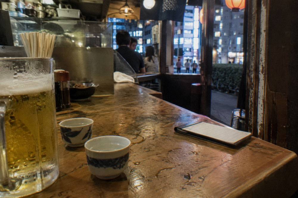 Two small glasses of sake and a beer on a wooden izakaya counter