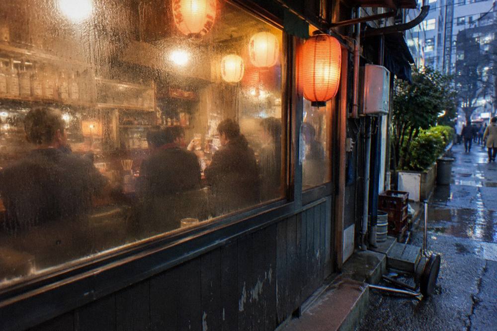 A guide raising a glass with a small group at a lantern-lit izakaya counter