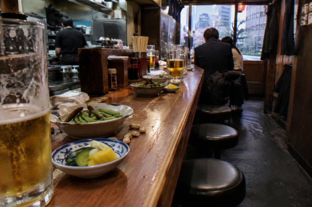 Small dishes and glasses of beer lined along a wooden izakaya counter
