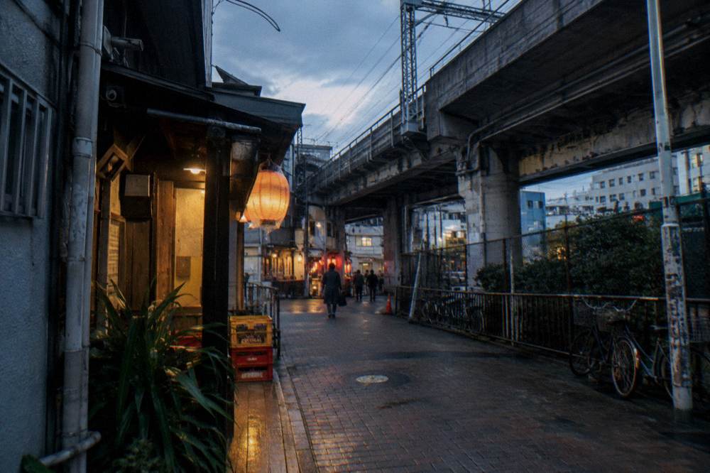 A Tokyo alley at dusk with warm light spilling from small bar doorways