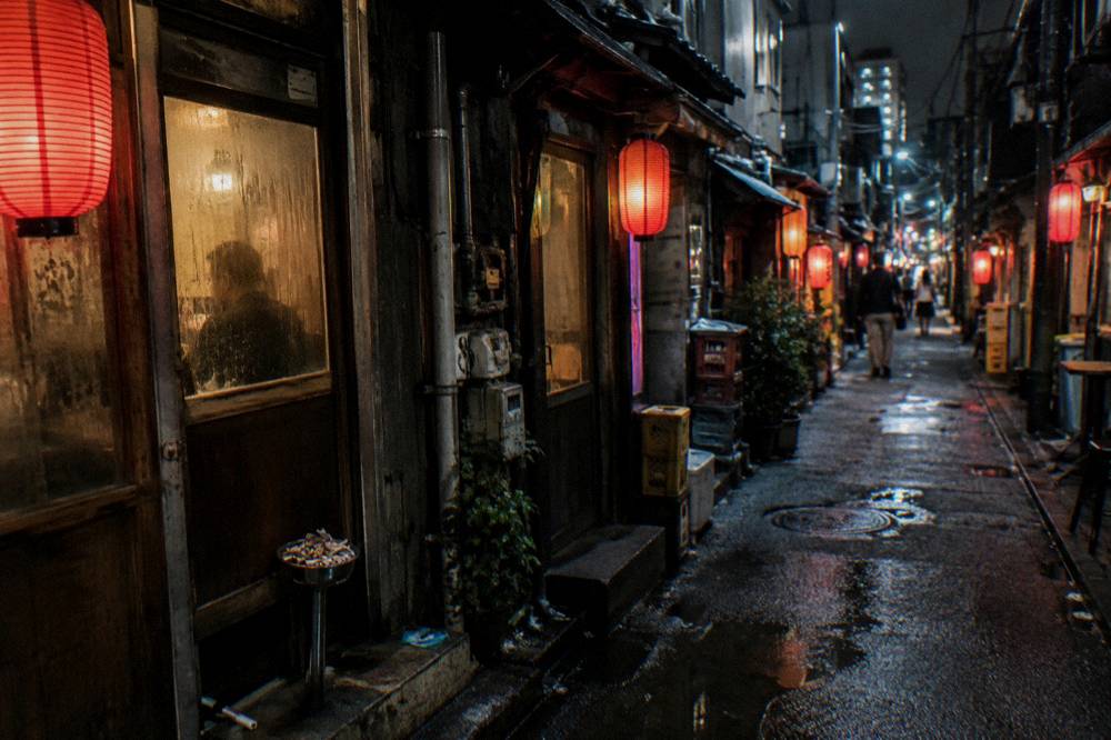 Rows of small red-lanterned bar fronts lining a narrow Golden Gai alley at night